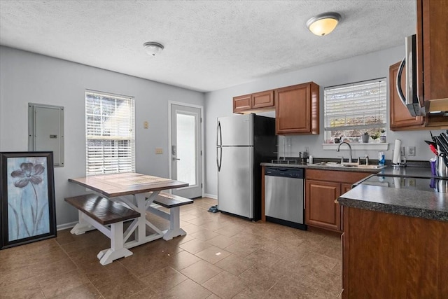 kitchen with brown cabinets, stainless steel appliances, dark countertops, a healthy amount of sunlight, and a sink