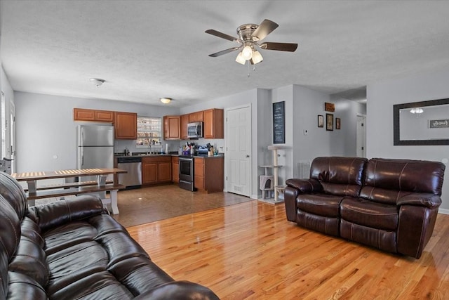 living area featuring a ceiling fan, light wood-style flooring, and a textured ceiling