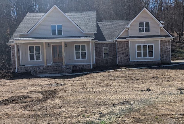 view of front of property with a porch, french doors, brick siding, and roof with shingles