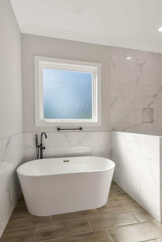 full bathroom featuring wood finish floors, a freestanding tub, tile walls, and crown molding