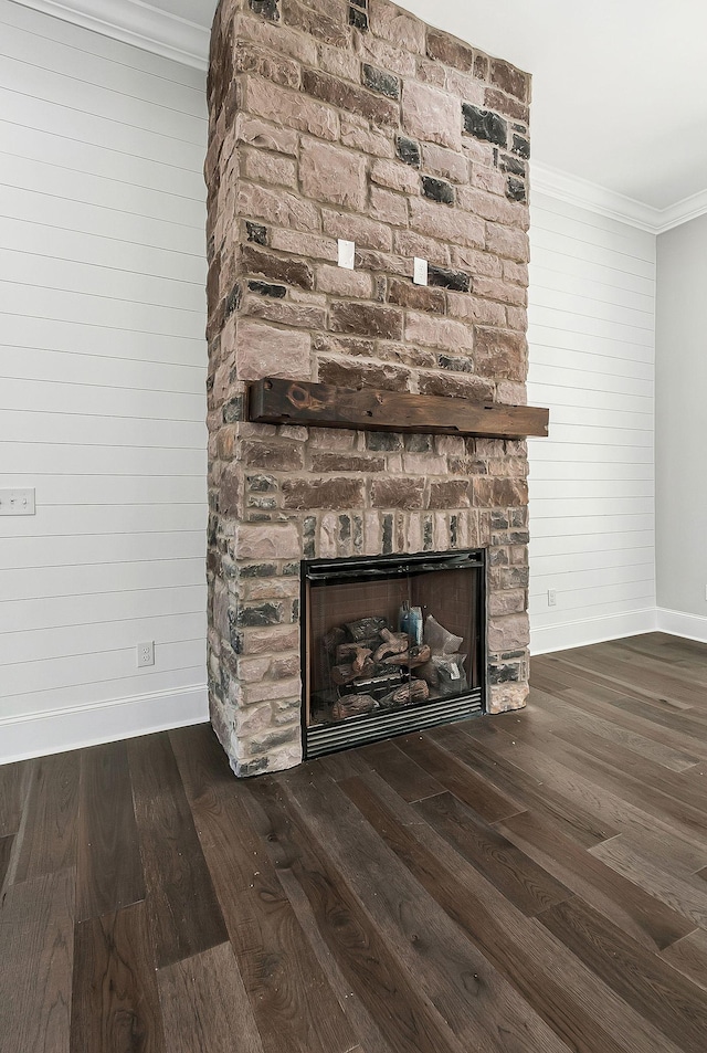 room details with a stone fireplace, wood walls, wood finished floors, baseboards, and crown molding