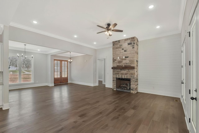 unfurnished living room with a stone fireplace, ceiling fan with notable chandelier, baseboards, ornamental molding, and dark wood-style floors