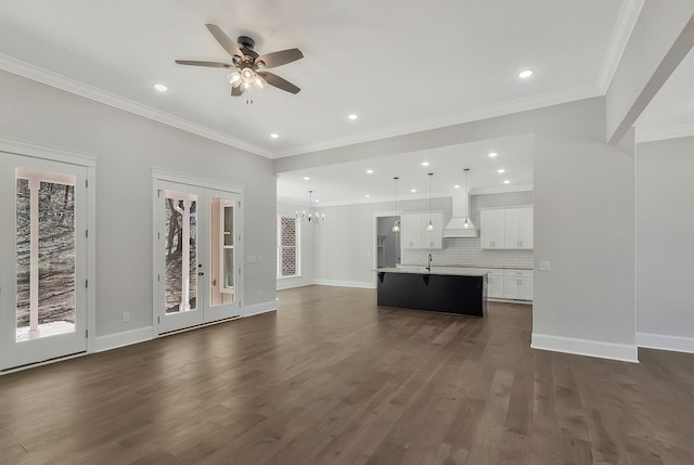 unfurnished living room featuring ceiling fan with notable chandelier, dark wood-type flooring, a sink, baseboards, and crown molding