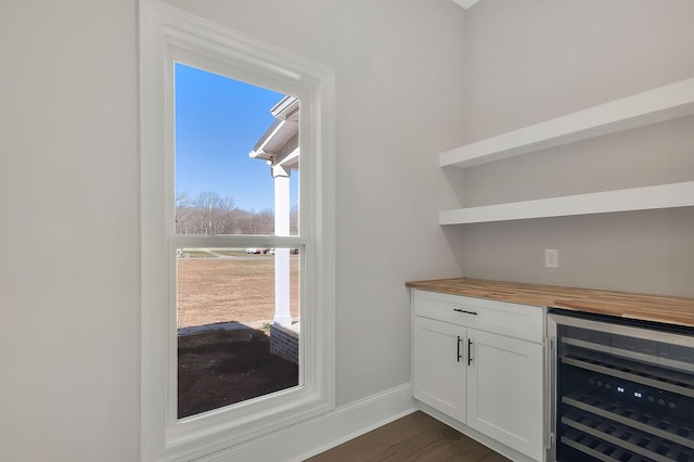 bar with beverage cooler, dark wood-type flooring, and baseboards