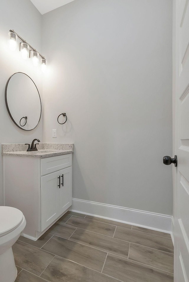 bathroom with toilet, wood tiled floor, baseboards, and vanity