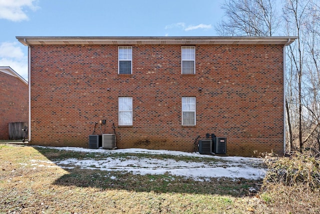 snow covered back of property with brick siding and central air condition unit