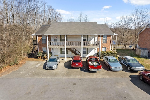 view of front facade featuring uncovered parking, brick siding, stairway, and roof with shingles