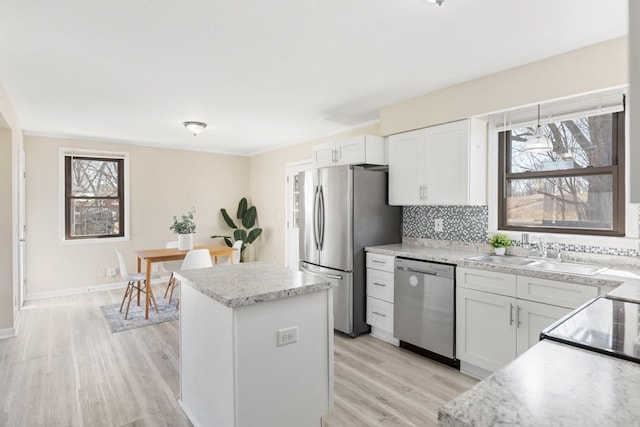 kitchen featuring a center island, light wood finished floors, stainless steel appliances, backsplash, and a sink