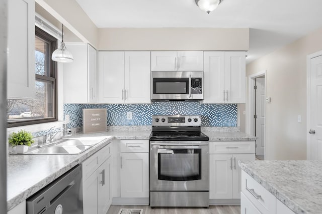 kitchen featuring stainless steel appliances, a sink, white cabinets, hanging light fixtures, and tasteful backsplash