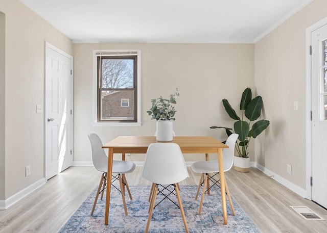 dining area featuring light wood finished floors, baseboards, visible vents, and ornamental molding