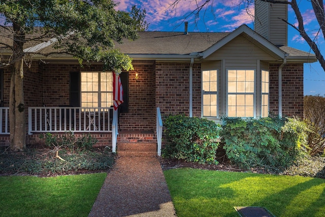 view of front of property featuring covered porch, brick siding, a chimney, and a front lawn