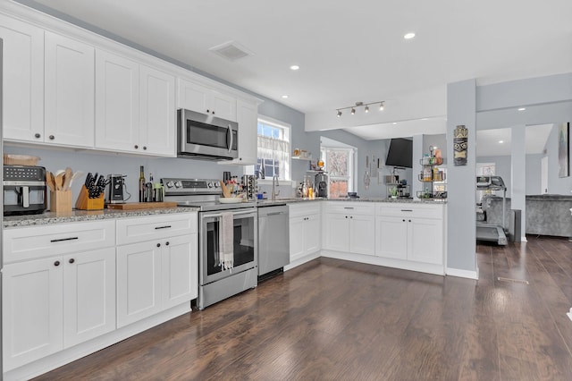 kitchen featuring white cabinetry, appliances with stainless steel finishes, open floor plan, and dark wood-type flooring