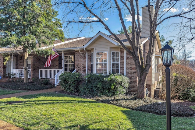 view of front facade featuring a porch, a chimney, a front yard, and brick siding