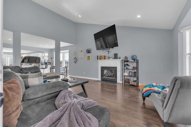 living area featuring dark wood-style floors, a fireplace with flush hearth, baseboards, and vaulted ceiling