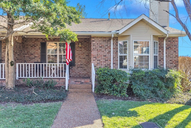 view of front of house with a chimney, brick siding, a front lawn, and a porch