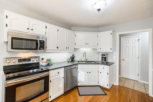 kitchen featuring backsplash, light wood-style flooring, appliances with stainless steel finishes, white cabinets, and a sink