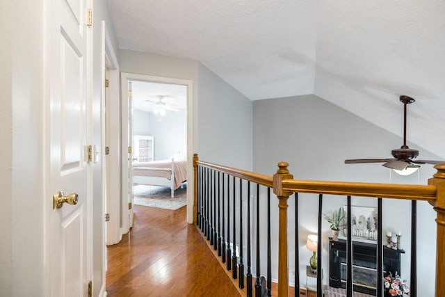 hall with lofted ceiling, hardwood / wood-style floors, a textured ceiling, and an upstairs landing