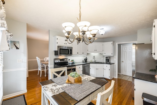 kitchen featuring stainless steel appliances, dark countertops, tasteful backsplash, white cabinetry, and a sink