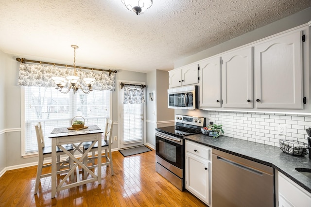 kitchen featuring stainless steel appliances, white cabinets, hanging light fixtures, light wood-type flooring, and dark countertops