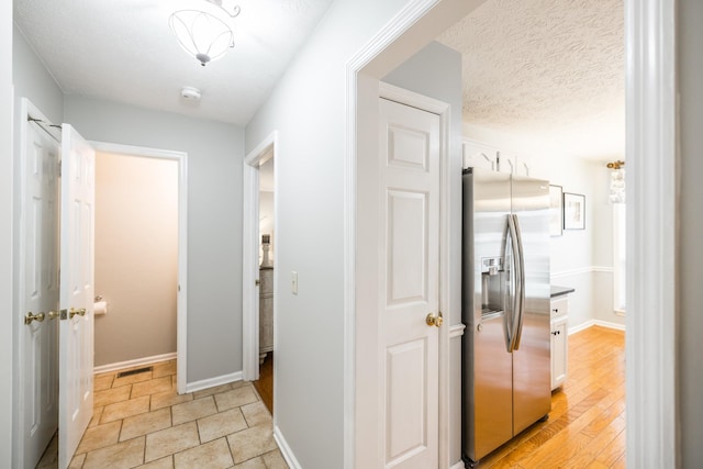 corridor with light wood finished floors, visible vents, baseboards, and a textured ceiling