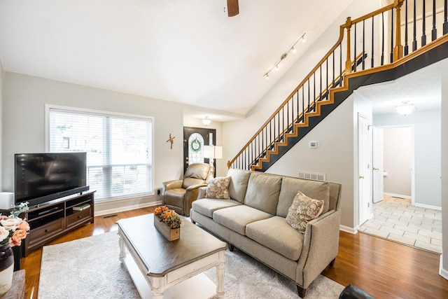 living room featuring wood finished floors, visible vents, baseboards, and stairs