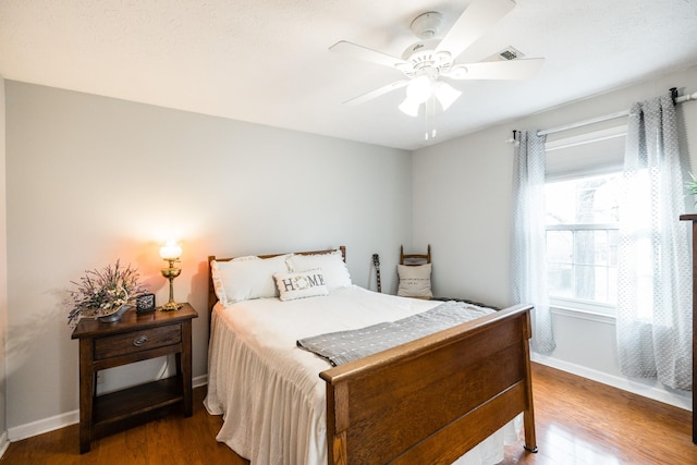 bedroom with a ceiling fan, wood finished floors, visible vents, and baseboards