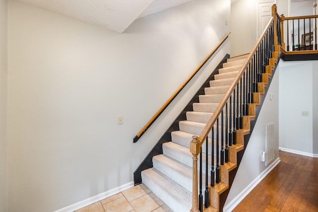 staircase featuring visible vents, a textured ceiling, baseboards, and wood finished floors