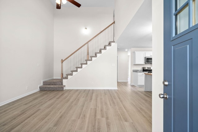 foyer entrance with stairs, light wood finished floors, a high ceiling, and baseboards