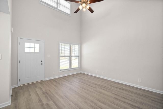 interior space with light wood finished floors, a high ceiling, baseboards, and a wealth of natural light