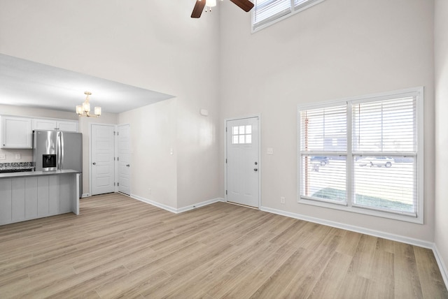 foyer with light wood-style flooring, baseboards, and ceiling fan with notable chandelier