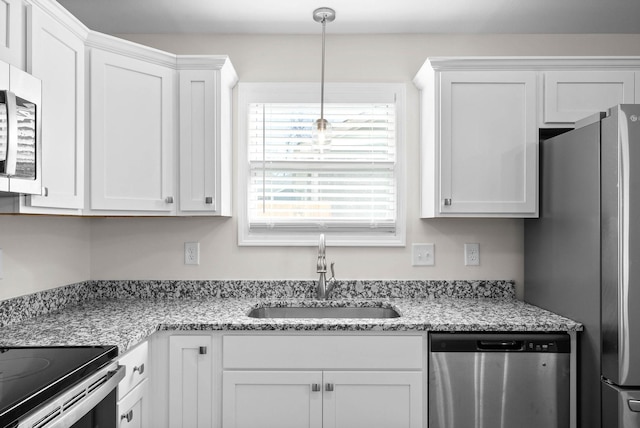 kitchen with stainless steel appliances, a sink, white cabinetry, hanging light fixtures, and light stone countertops