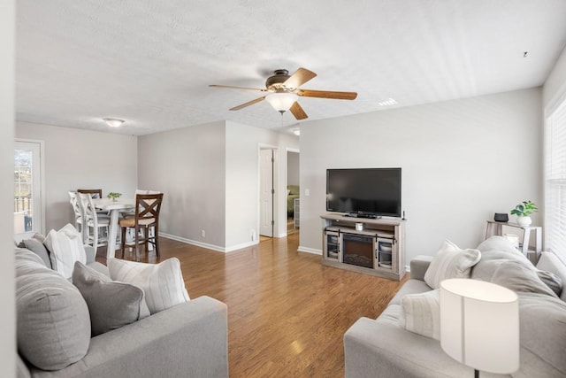 living room featuring a textured ceiling, wood finished floors, a ceiling fan, and baseboards