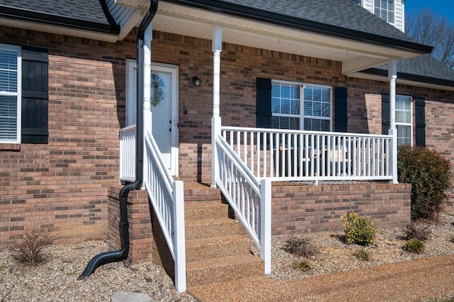 property entrance with covered porch, a shingled roof, and brick siding