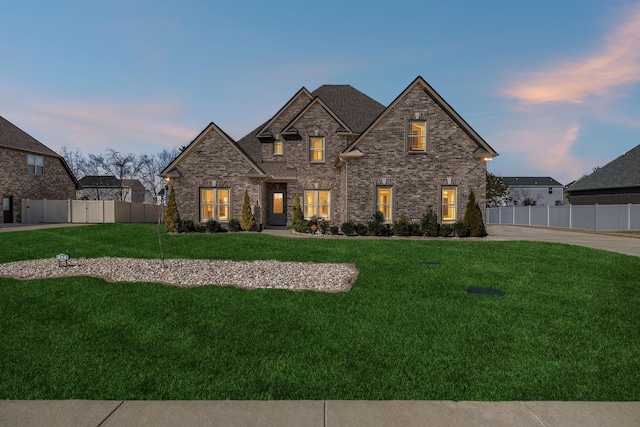 french country home featuring a front yard, fence, and brick siding