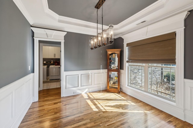 unfurnished dining area with a tray ceiling, a wainscoted wall, visible vents, wood finished floors, and washer and dryer