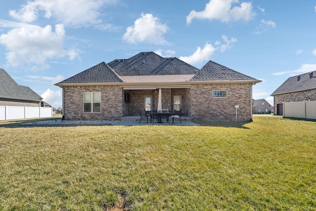 rear view of property with a patio, roof with shingles, fence, a yard, and brick siding