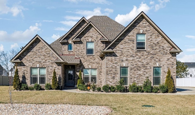 craftsman-style house featuring a front yard, brick siding, fence, and roof with shingles