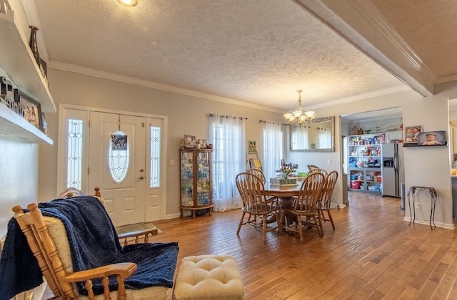 dining space with a textured ceiling, baseboards, hardwood / wood-style floors, an inviting chandelier, and crown molding