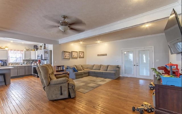 living room with a ceiling fan, ornamental molding, a textured ceiling, french doors, and light wood-type flooring