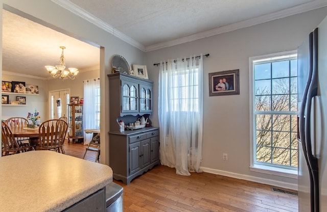 dining room featuring light wood-type flooring, an inviting chandelier, baseboards, and crown molding