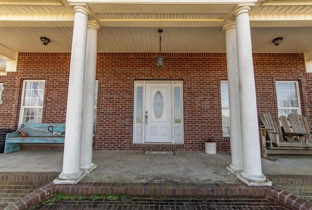 view of exterior entry featuring brick siding and a porch