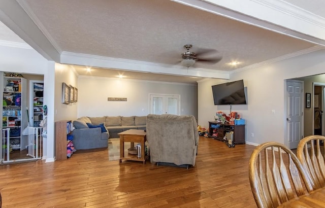 living room featuring light wood-style floors, ornamental molding, a ceiling fan, a textured ceiling, and baseboards