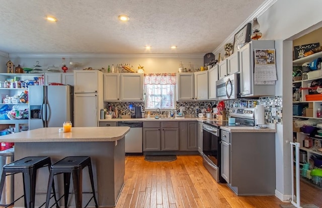 kitchen with a kitchen island, gray cabinets, stainless steel appliances, light countertops, and a sink