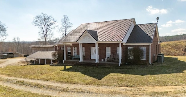 view of front facade with metal roof, cooling unit, covered porch, brick siding, and a front lawn