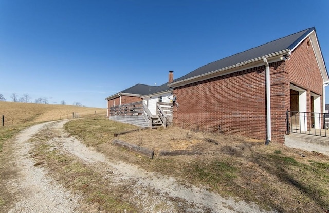 view of side of home with brick siding, a rural view, a chimney, and fence