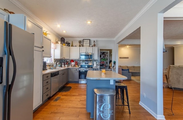 kitchen featuring a kitchen island, gray cabinets, stainless steel appliances, light countertops, and a kitchen bar