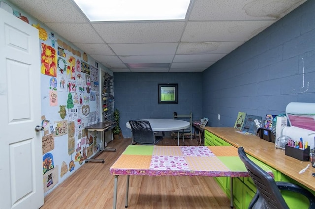 recreation room featuring a paneled ceiling, wood finished floors, and concrete block wall