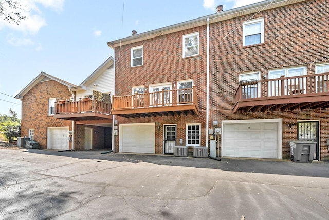 back of house featuring a garage, driveway, brick siding, and cooling unit