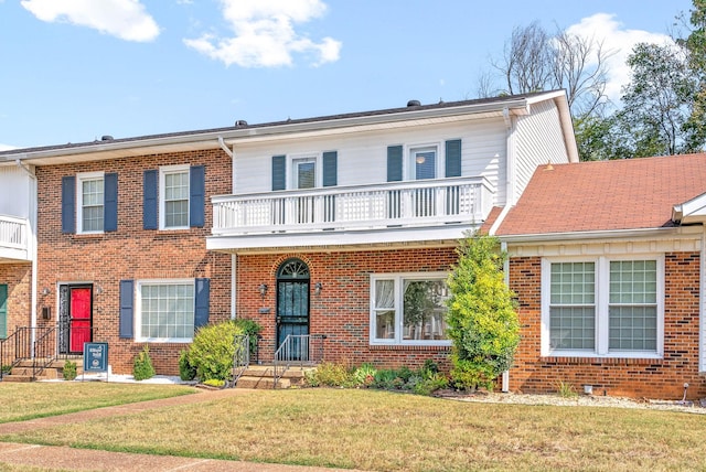 view of front of property featuring a balcony, brick siding, and a front yard