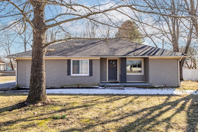 ranch-style home with a shingled roof, a chimney, a front lawn, and brick siding